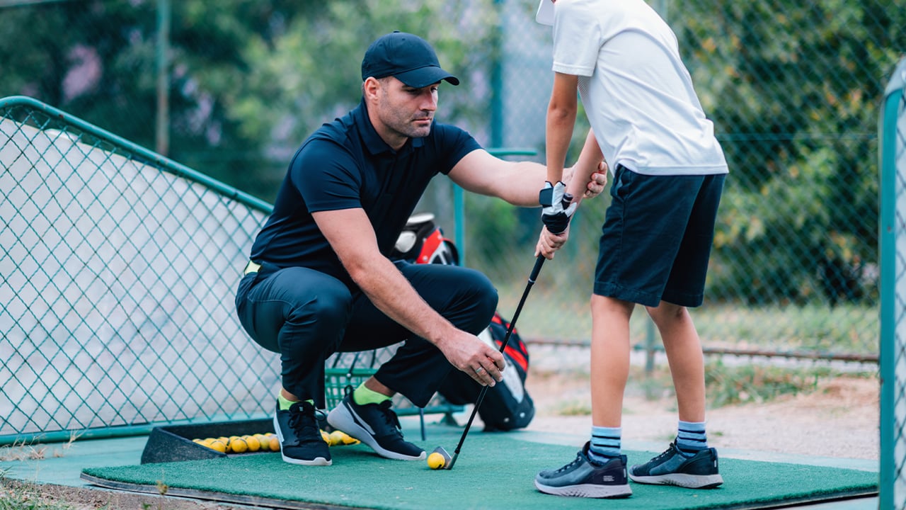 Golf Instructor teaches a young boy how to swing at a driving range